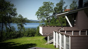 A wooden cabin with a deck overlooking a lake, surrounded by trees.