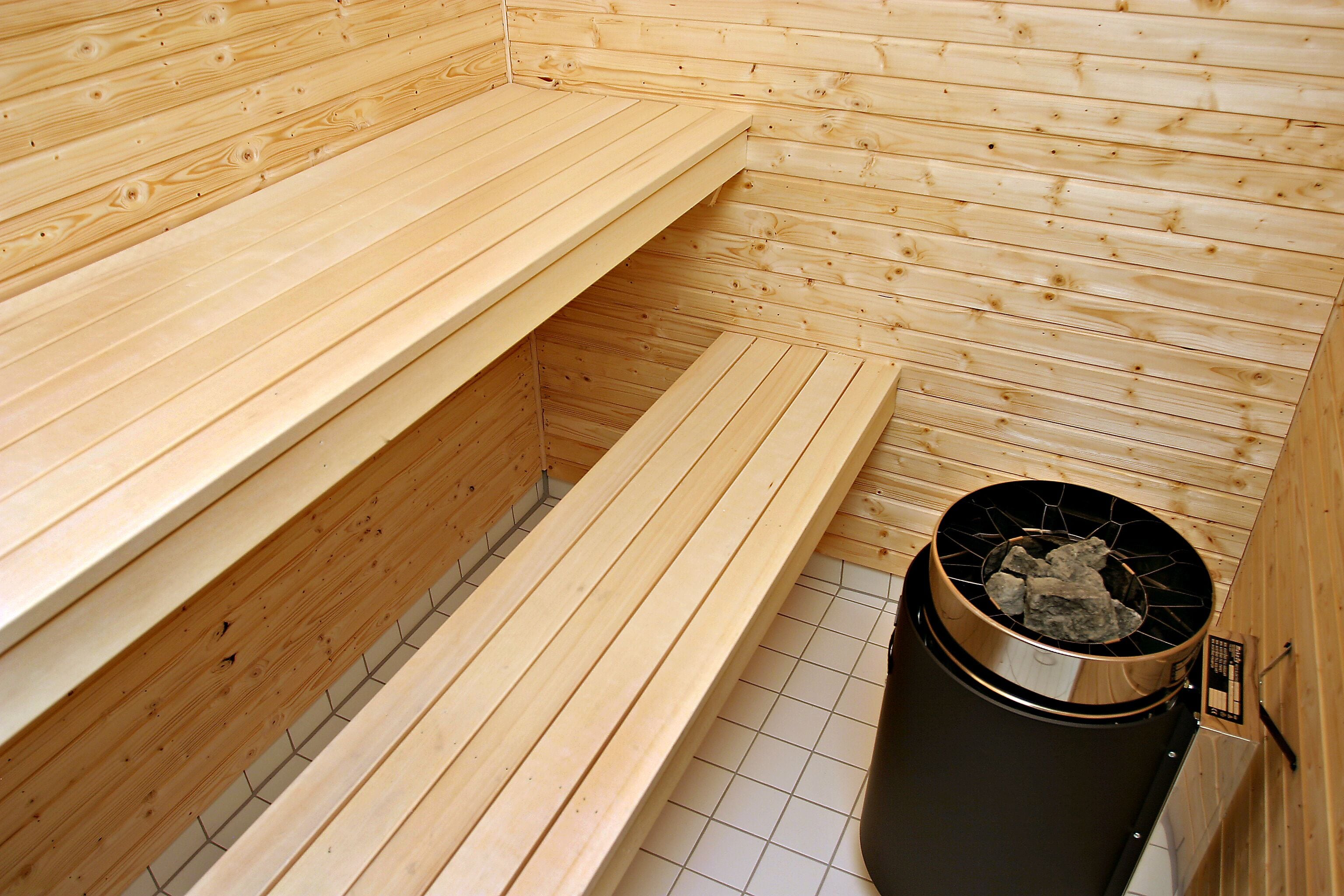 A sauna with wooden benches and a black trash bin.