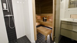 A sauna with a wooden bench, a black bucket, and a showerhead.