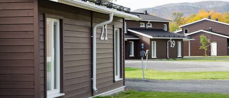 A row of brown wooden houses with white trim, numbered 19, in a residential area with a mountain backdrop.