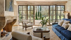 A spacious living room with a fireplace, a blue sofa, a wooden chair, and a glass coffee table. - Spectacular unique villa in the Emporda (Calabuig)