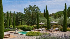 A pool area with lounge chairs and umbrellas, surrounded by neatly trimmed hedges and tall trees. - Spectacular unique villa in the Emporda (Calabuig)