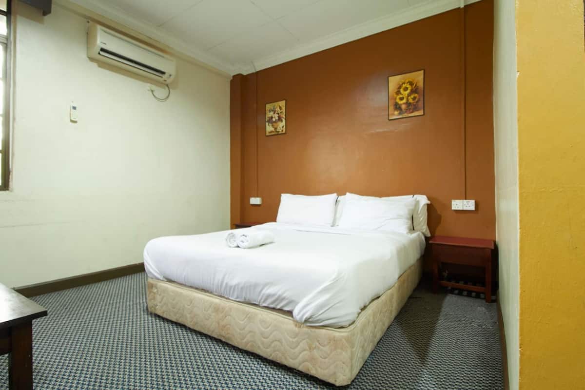 Une chambre d’hôtel avec un lit simple, une petite table de chevet, un appareil de climatisation et une moquette à motifs.