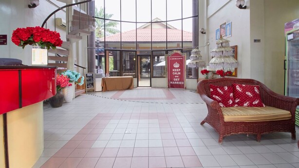 A hotel lobby with a reception desk, a wicker sofa, a staircase, and a glass door entrance. - D'Jawi Bella Hotel (Sungai Jawi)