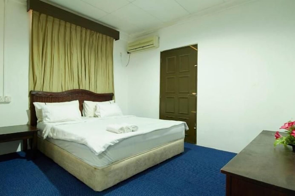 A hotel room with a single bed, a wooden headboard, a blue carpet, a wooden nightstand, and a door.