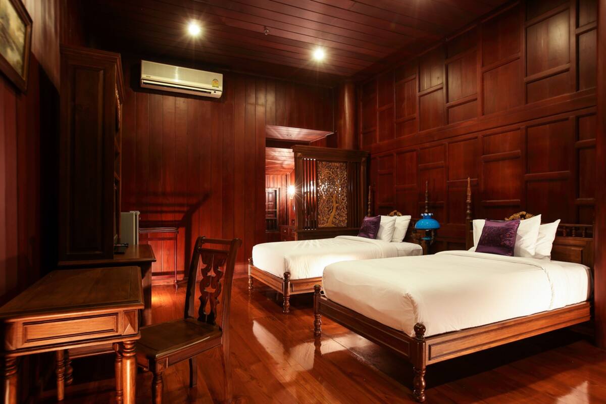 Une chambre d’hôtel avec deux lits en bois, un bureau en bois et une chaise.