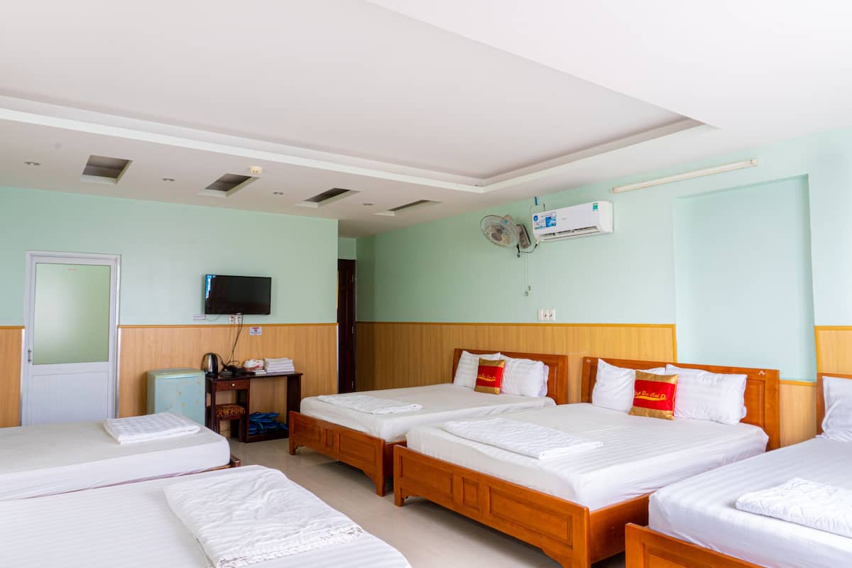 A hotel room with two single beds, a television, a small refrigerator, and a wooden nightstand.