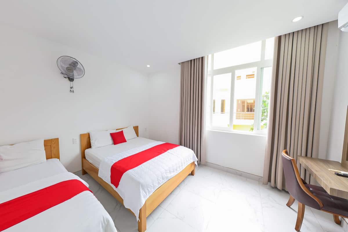 A hotel room with two beds, a desk, and a window with curtains.