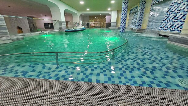 Ein Hallenbad mit Schachbrettboden, einer zentralen Insel und einer Wassersäule.