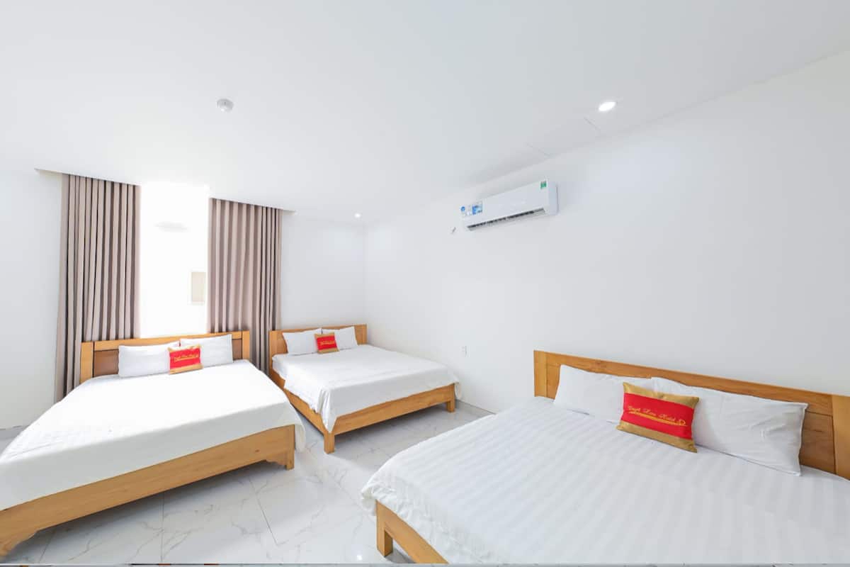 A hotel room with three single beds, a white air conditioning unit on the wall, and a window with curtains.