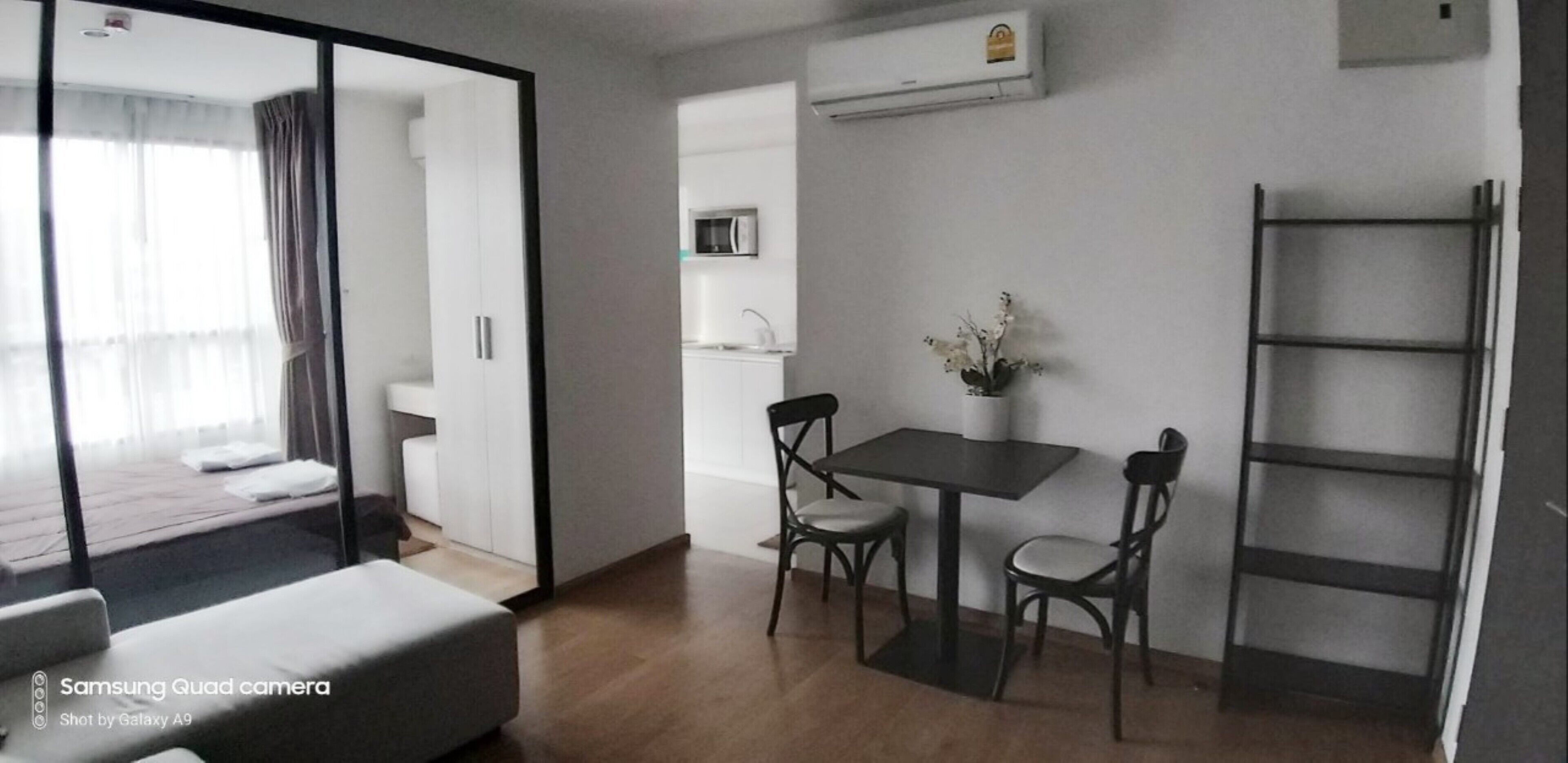 Ein modernes Zimmer mit einem Bett, einem Esstisch mit Stühlen, einer kleinen Küchenzeile und einer eingebauten Regalanlage.