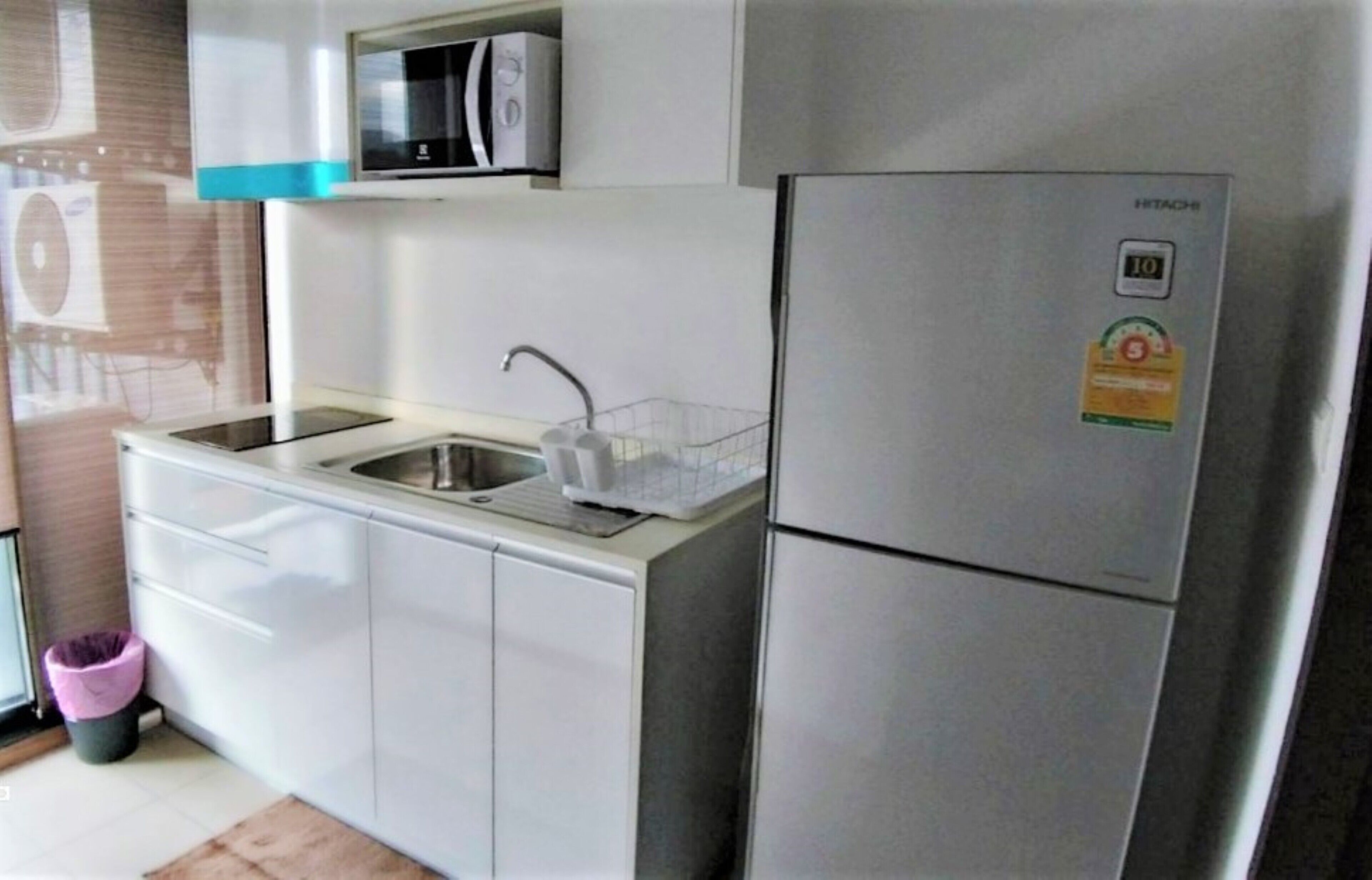 A modern kitchen with white cabinets, a stainless steel refrigerator, a microwave, and a sink with a faucet.