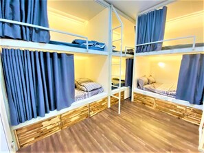 Ein Schlafsaalzimmer mit Etagenbetten, Holzboden und Vorhängen.