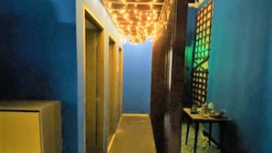 Un couloir étroit aux murs bleus et au plancher en bois. Une table, sur laquelle se trouvent divers objets, est placée sur le côté droit, et une porte se trouve au fond du couloir.