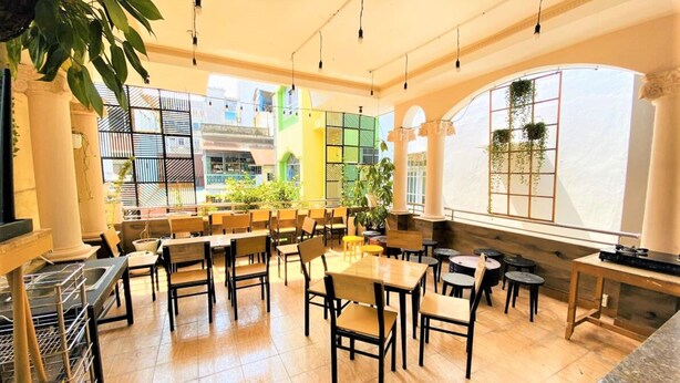 Un vaste espace de restauration intérieur, doté de nombreuses tables et chaises, de grandes fenêtres offrant une vue sur les bâtiments et de plantes suspendues.