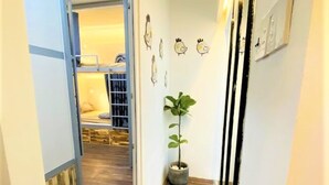 Un couloir étroit qui mène à une pièce avec un lit superposé, une plante en pot et des décorations murales.