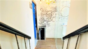 Un escalier avec des marches en bois et des rampes noires, menant à une pièce dont un mur est orné d’une grande fresque.