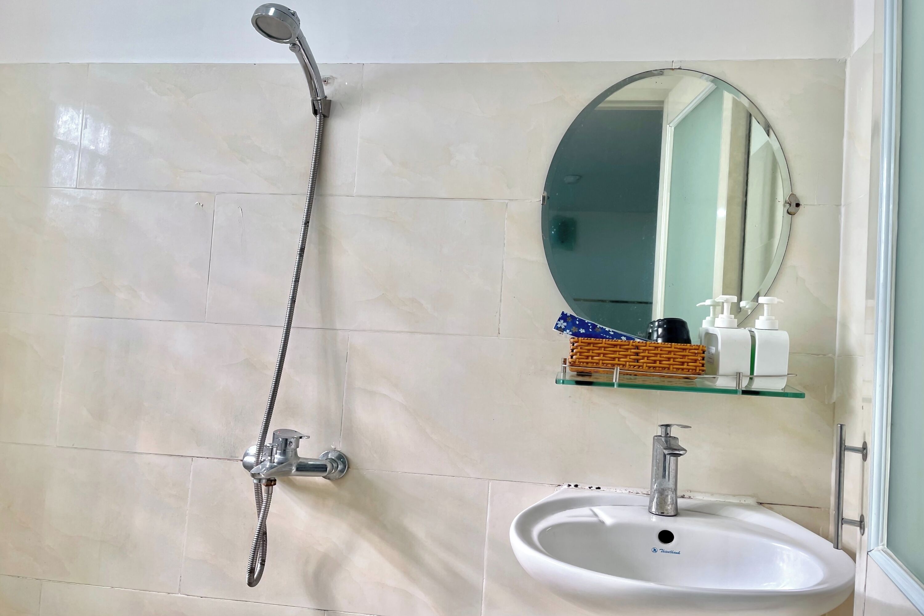 Een badkamer met een douche, wastafel, spiegel en toiletartikelen op een plank.