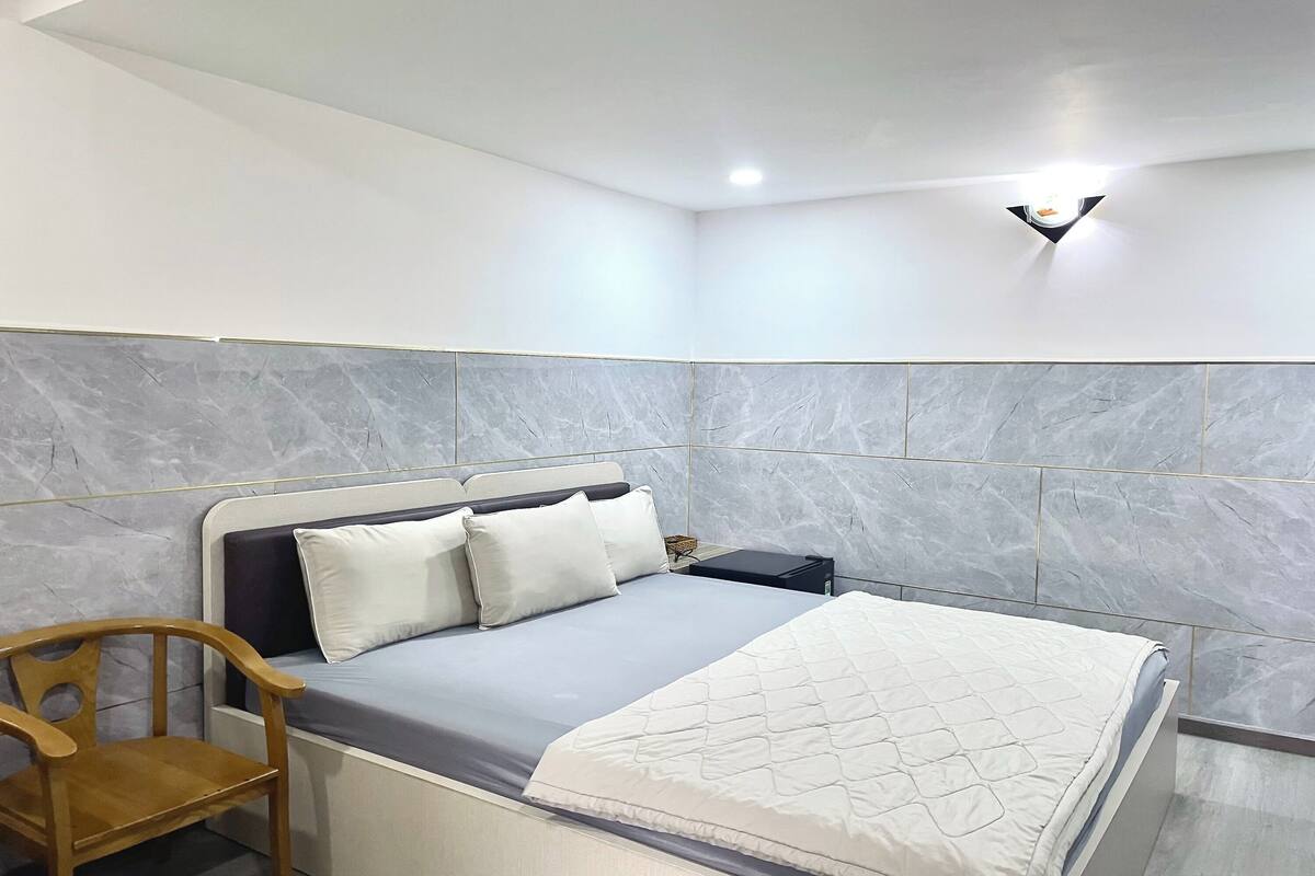 Een slaapkamer met een bed, een nachtkastje, een stoel en een wandlamp.