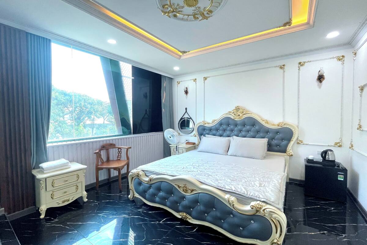 Een slaapkamer met een groot bed, nachtkastje, stoel en een klein tafeltje met waterkoker.