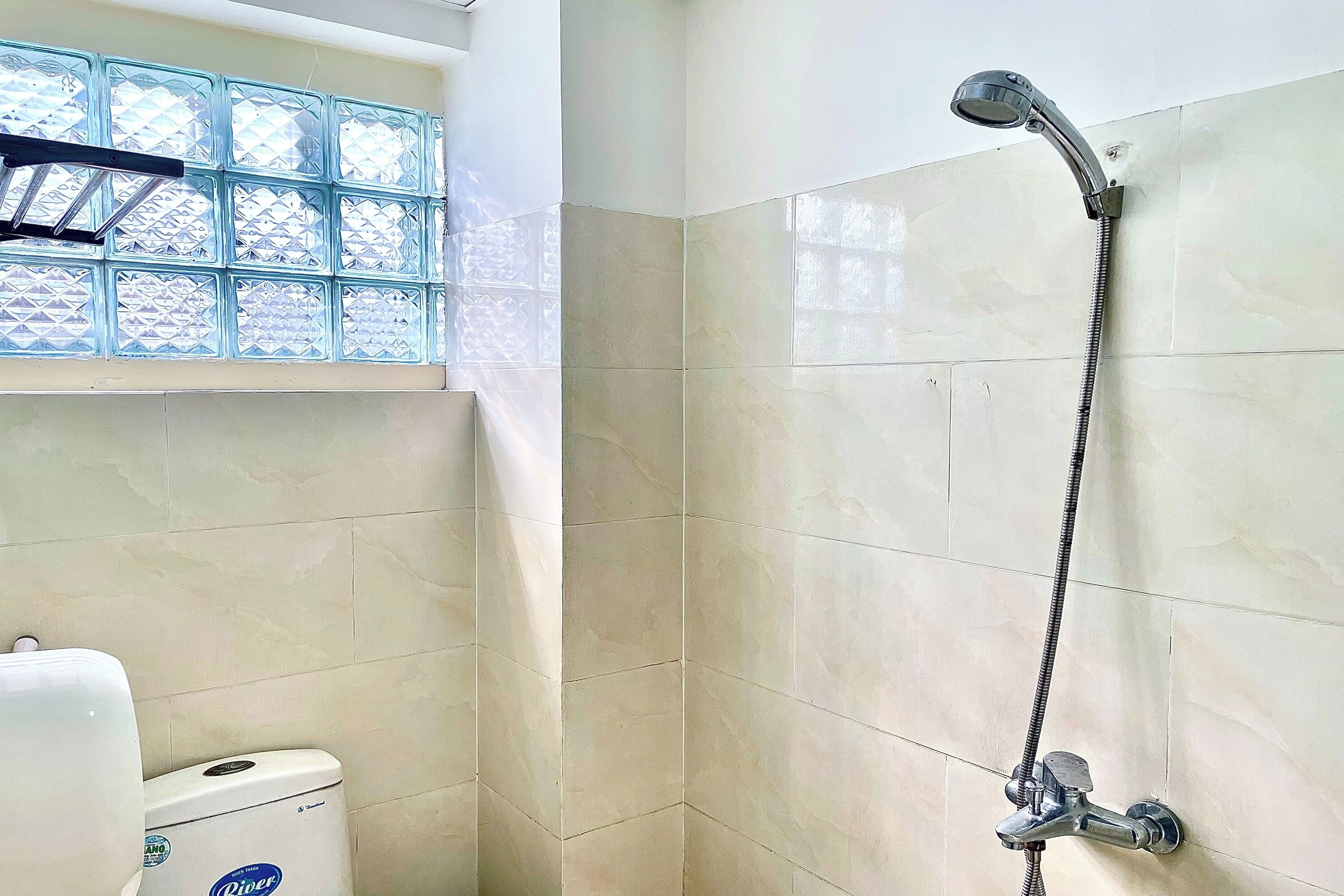 A bathroom with a toilet, a shower with a handheld showerhead, and a window with frosted glass.