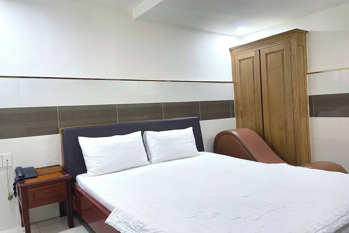Een hotelkamer met een bed, een houten garderobe, een nachtkastje met een telefoon en een bruine stoel.