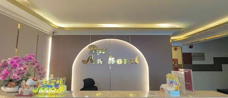 A hotel reception desk with a sign reading 'An Hotel,' a decorative vase with flowers, and a small statue.