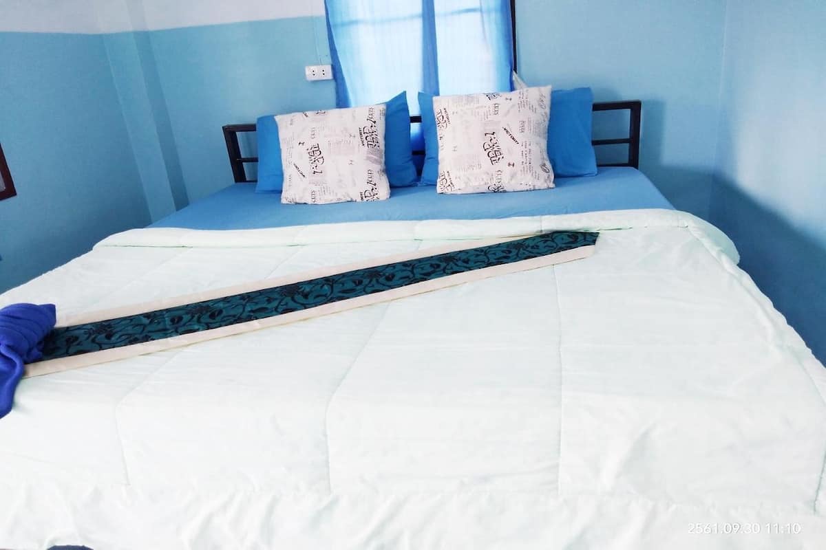 Un lit avec une couette blanche, deux oreillers bleus et une tête de lit en bois.
