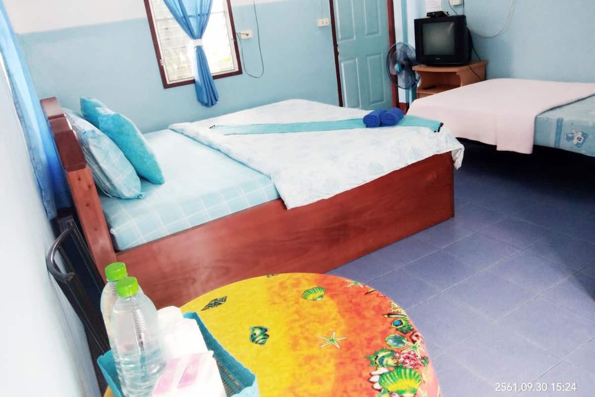 Une chambre avec un lit, une télévision, un ventilateur et une table sur laquelle se trouvent des bouteilles.