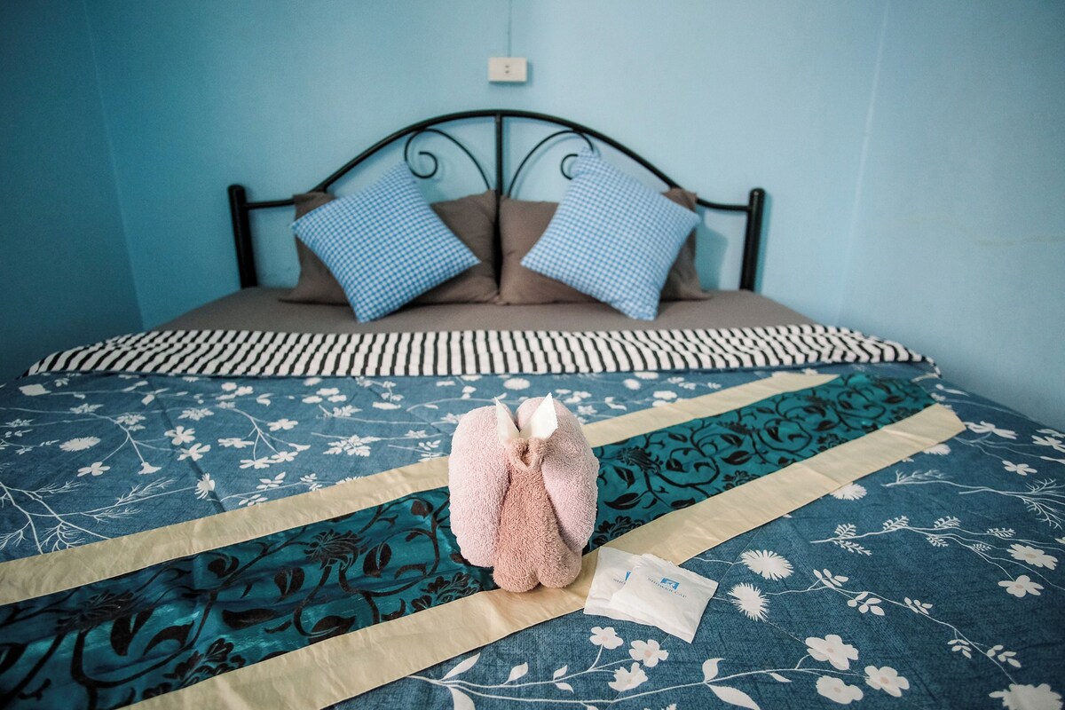 A bed with a floral bedspread, two pillows, and a pair of slippers on the bed.