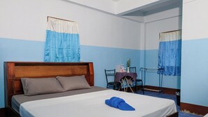 Un dormitorio con cama de madera, una mesita con silla y una ventana con cortinas azules.