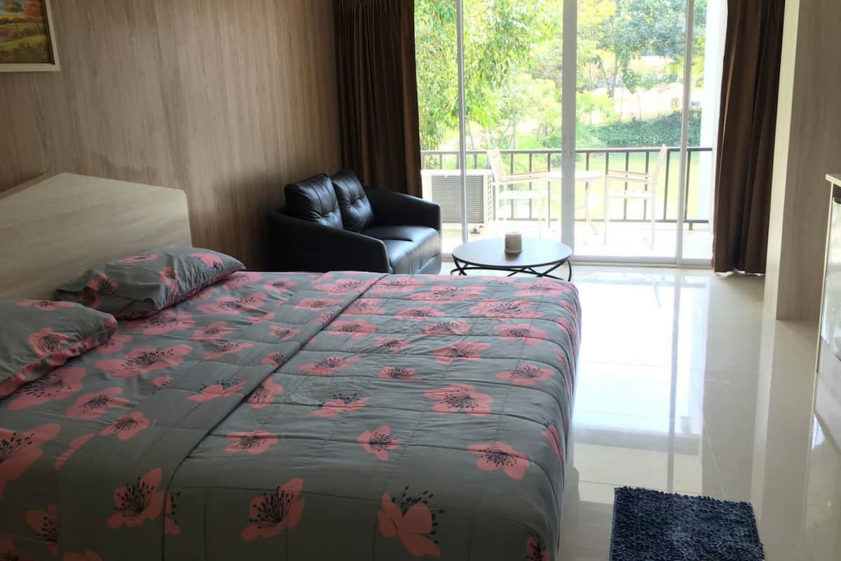 Un dormitorio con una cama grande, una silla, una mesita y un balcón con vistas a la vegetación.