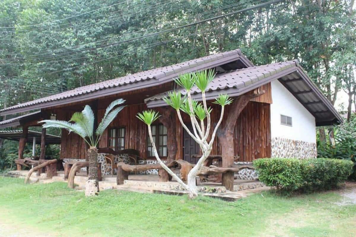 Una casa de madera rústica con techo de tejas, rodeada de abundante vegetación y un césped cuidado.