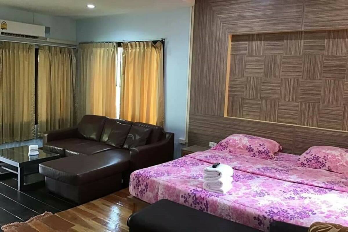 Una habitación de hotel moderna con un sofá de cuero marrón, una mesa de centro de vidrio, una cama con cubrecama floral rosa y una pared de acento de madera.