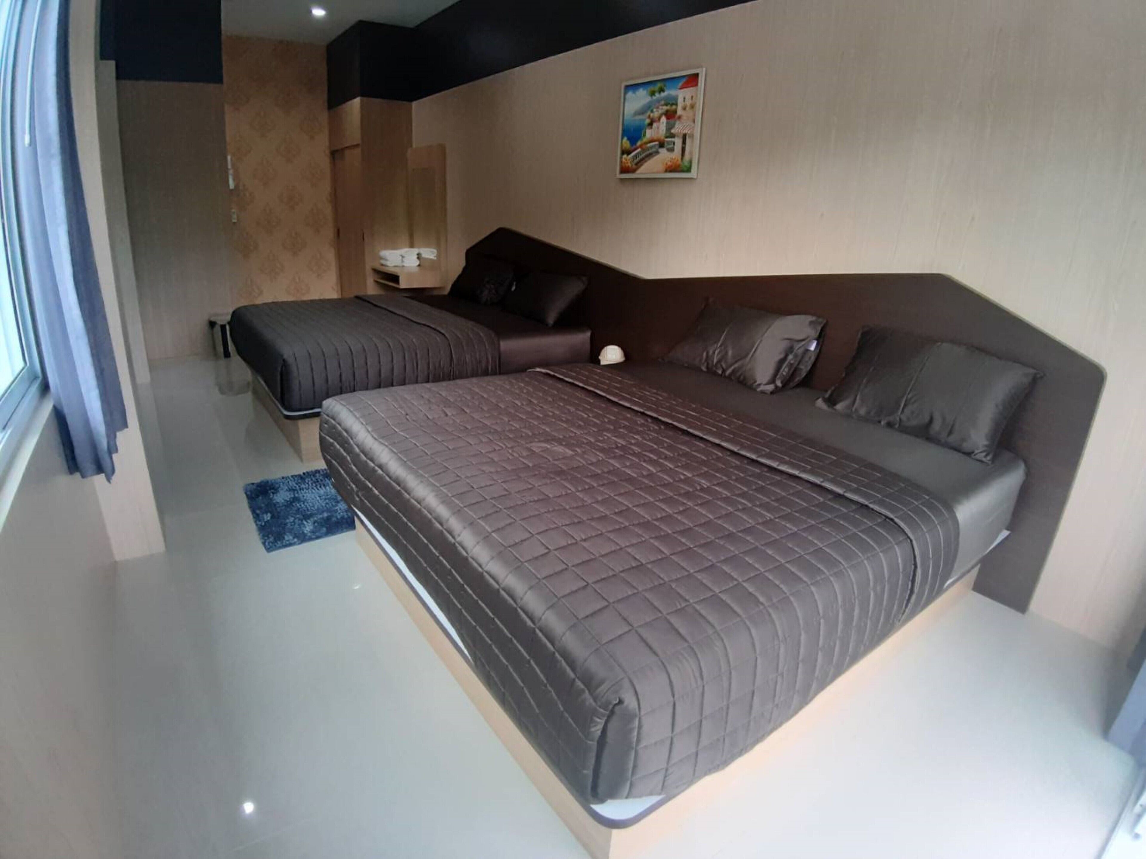 A modern bedroom with a large bed, a smaller bed, and a sofa. There is a painting on the wall and a window with curtains.