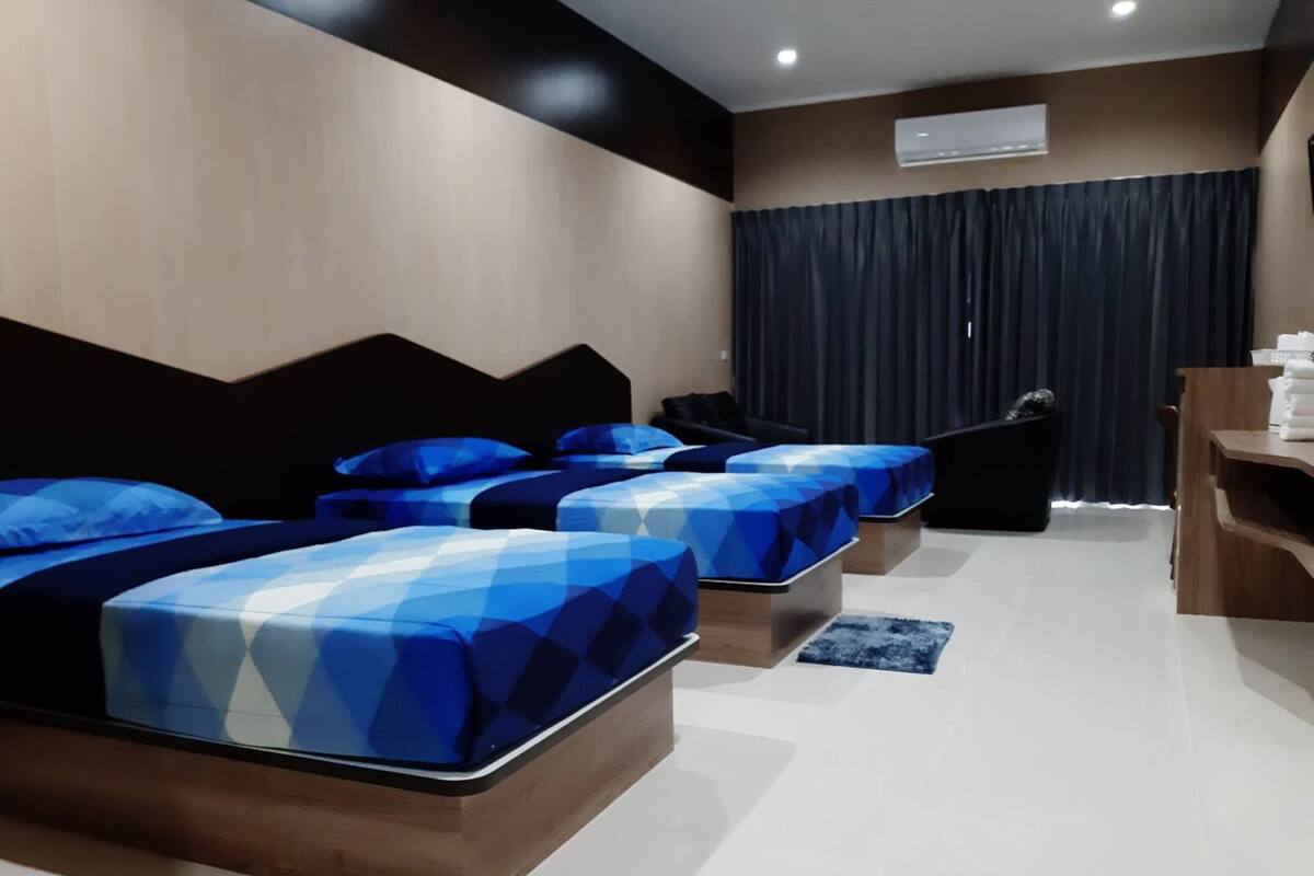 Habitación de hotel con diseño moderno, que incluye una cama grande con edredón estampado con motivos geométricos, una cama adicional, un escritorio con silla y un ventanal con cortinas oscuras.