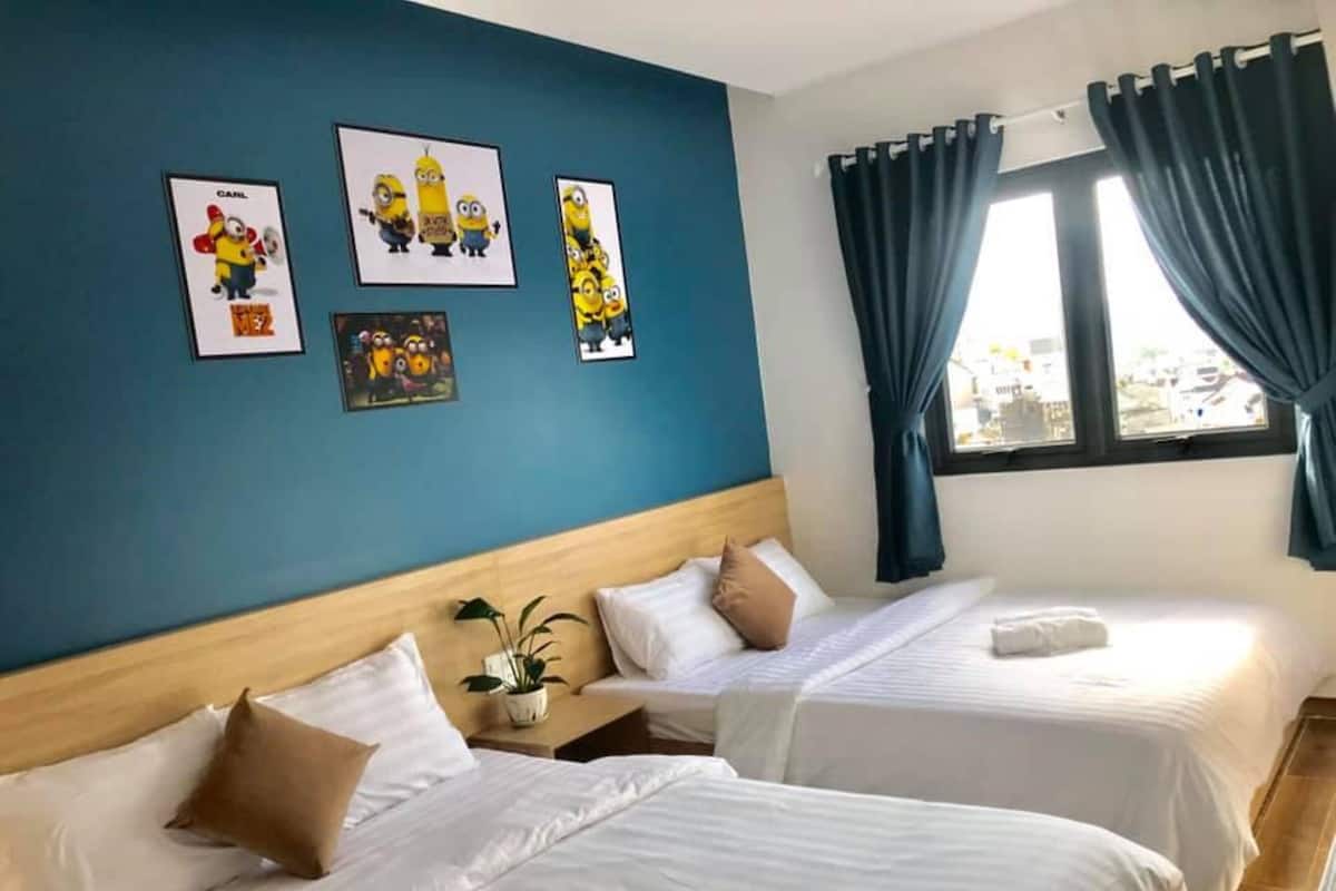 A hotel room with two beds, a large window with curtains, and wall art featuring cartoon characters.