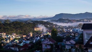 Un pueblo con viviendas densas, un edificio destacado que emite vapor y una cadena montañosa al fondo.