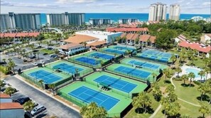 A resort with multiple tennis courts, a parking area, and a view of the ocean.