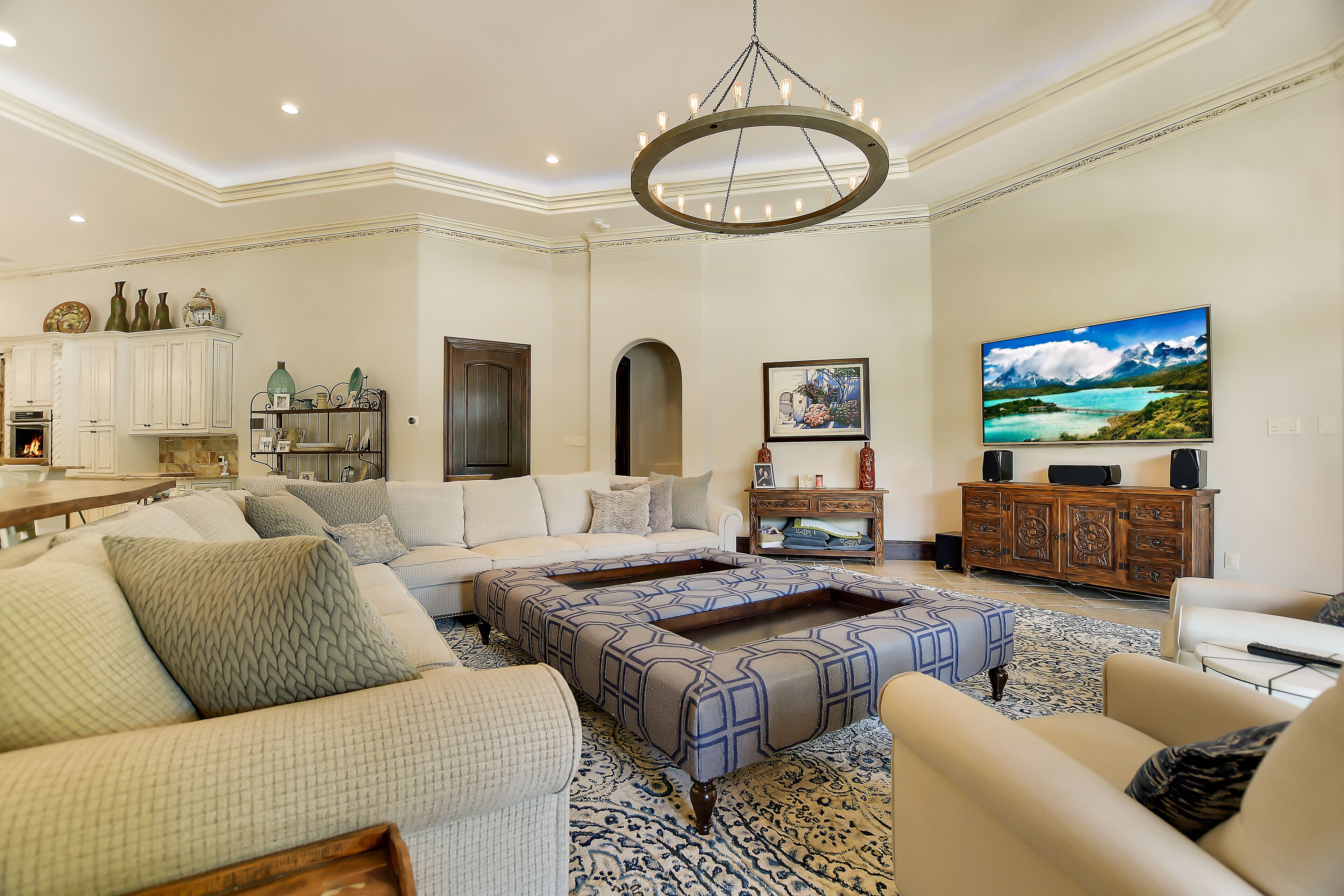 Un salon spacieux avec un grand canapé, un pouf à motifs, une table basse en bois et un téléviseur fixé au mur.