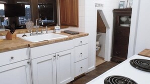 Une cuisine avec des meubles blancs, un plan de travail en bois, une cuisinière et un luminaire suspendu.