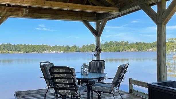 Une terrasse en bois avec une table et des chaises, donnant sur une étendue d’eau calme.