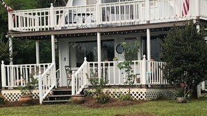 Une maison blanche à deux étages, dotée d’un porche, d’un drapeau et d’un petit jardin.