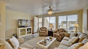 A living room with a television, two floral armchairs, a sofa, a coffee table, and a ceiling fan. - 146 The Shores (Panama City Beach)