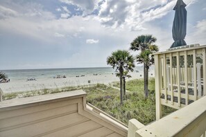 A beach view from a balcony with a railing, palm trees, and a statue.