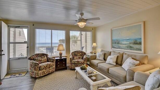 A living room with a ceiling fan, a sofa, two armchairs, a coffee table, and a painting on the wall. - 146 The Shores (Panama City Beach)