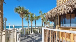 A wooden deck with a railing, palm trees, and a beach view. - Calypso Resort by BBG (Panama City Beach)