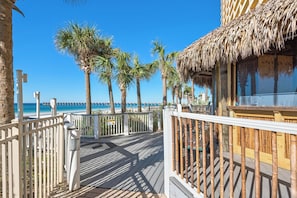 A wooden deck with a railing, palm trees, and a beach view. - Calypso Resort by BBG (Panama City Beach)