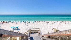 Une plage avec une promenade en bois menant au rivage, du sable blanc et une eau d’un bleu cristallin.