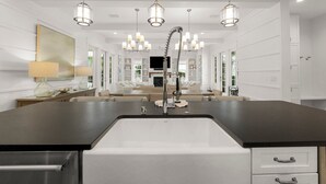 Une cuisine moderne dotée d’un grand îlot central, d’appareils électroménagers en acier inoxydable et de luminaires suspendus.